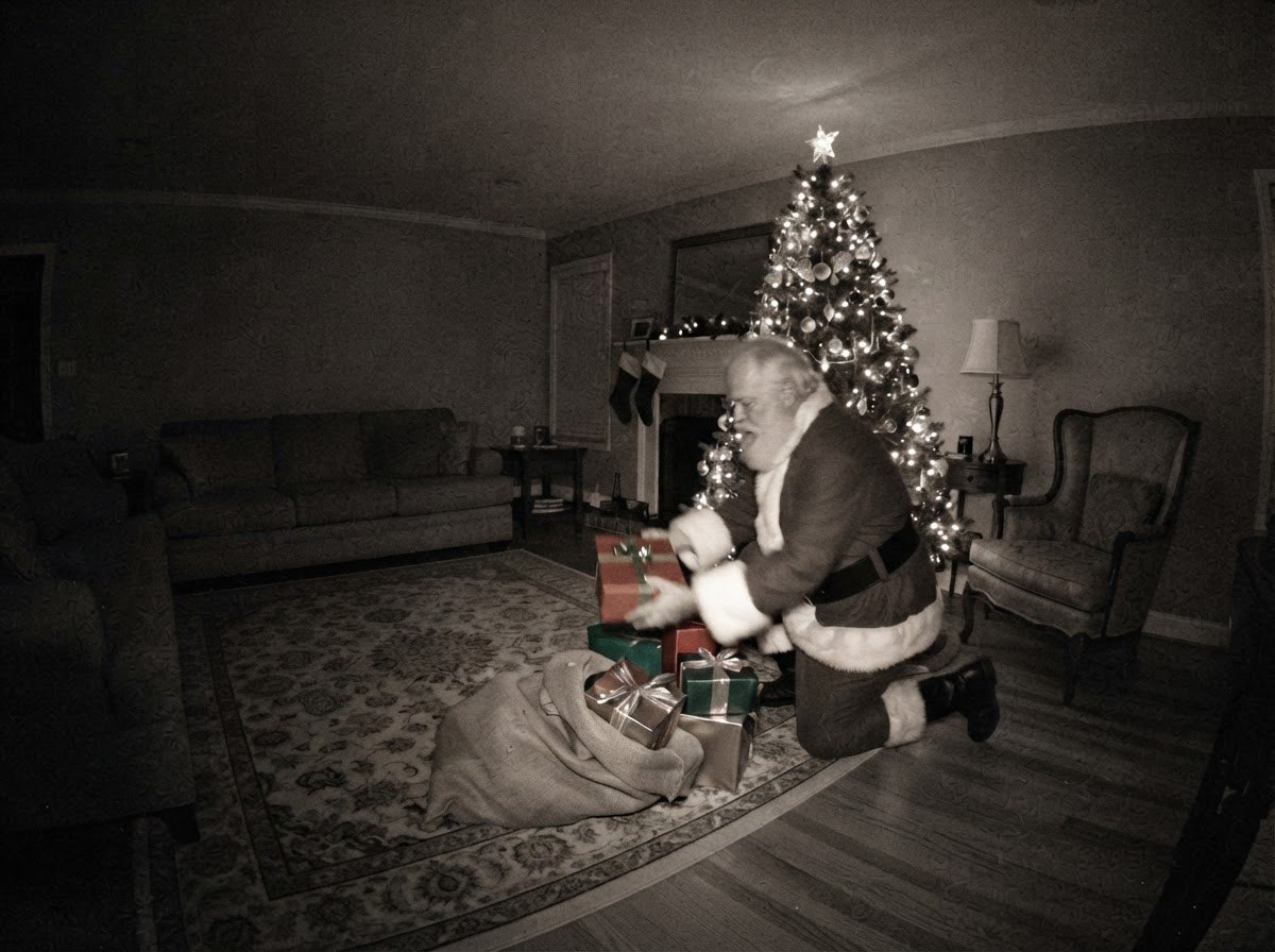 Santa caught on camera placing presents under the tree, second take — night-vision security camera still with CAM 01 label and timestamp